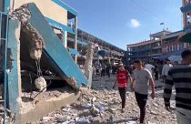 Pessoas caminham por entre os destroços de uma escola gerida pela UNRWA, atingida por um ataque israelita, 14 de julho de 2024
