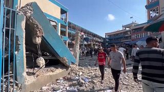 Pessoas caminham por entre os destroços de uma escola gerida pela UNRWA, atingida por um ataque israelita, 14 de julho de 2024