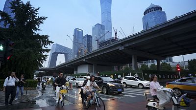 Peatones cruzan una intersección con el fondo del distrito central de negocios en Pekín, 12 de julio de 2024. 