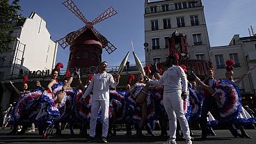 Des porteurs de la flamme olympique posent devant le Moulin Rouge pendant que des danseurs exécutent le French Cancan, lundi 15 juillet 2024 à Paris. 