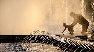 Un homme tient un enfant près d'une fontaine à Bucarest, en Roumanie, le vendredi 21 juin 2024, alors que les températures ont dépassé 35 °C.