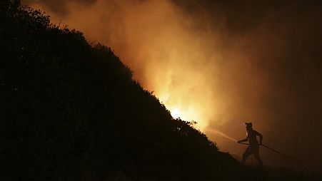 Un voluntario utiliza una manguera para tratar de combatir un incendio forestal cerca de casas en Portugal.