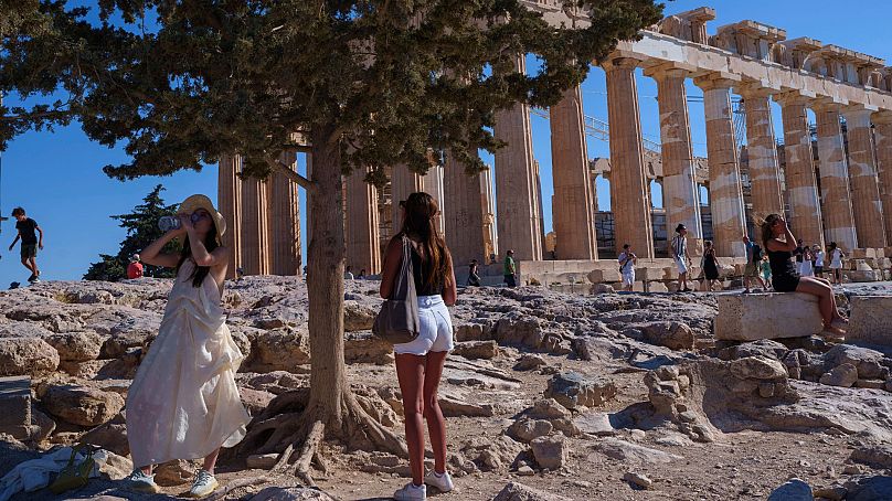 A woman drinks water in front of the ancient Parthenon Temple during a hot, windy day at Acropolis hill , in Athens, Tuesday, 16 July 2024. 