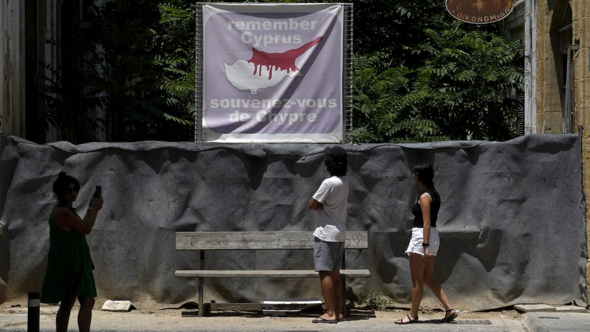 FILE -Tourist look at a road blocked with barrels and sand bags, with a banner showing the island in division at the top, 