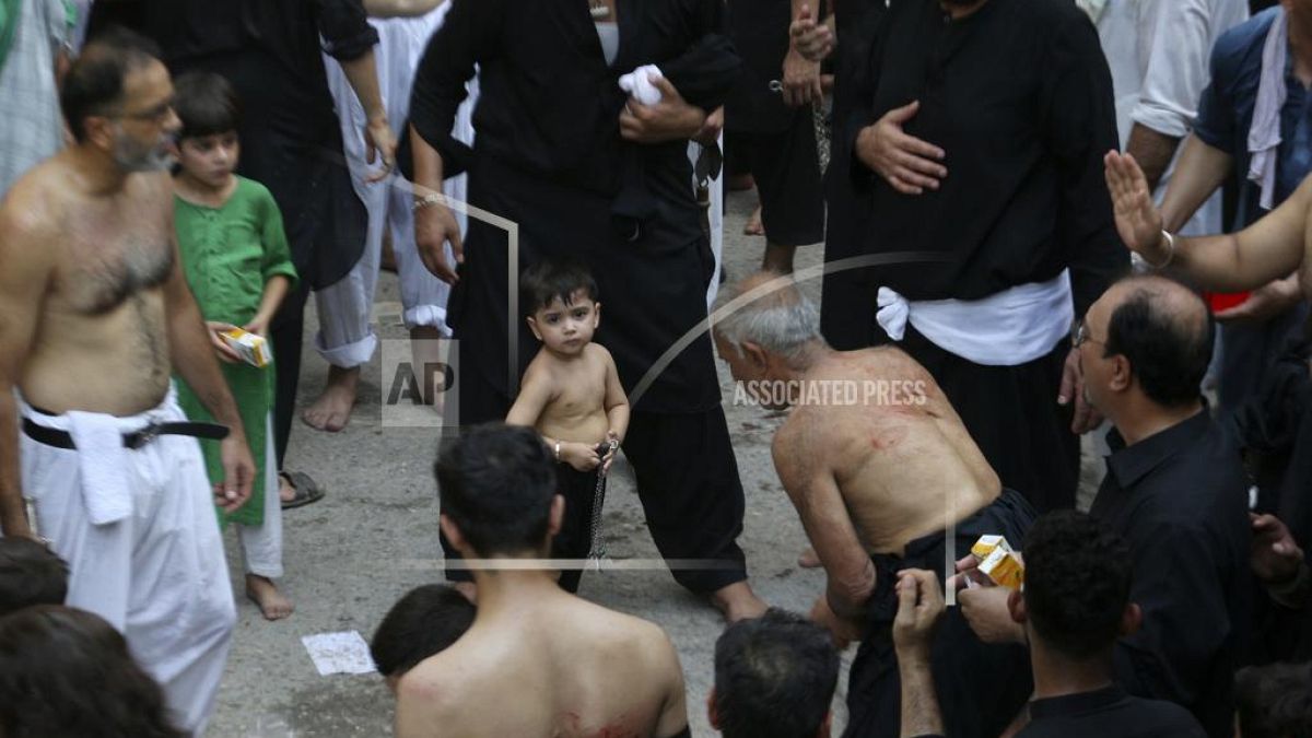 طفل شيعي يقف إلى جانب والده وسط حشد، إحياء لذكرى عاشوراء في باكستان