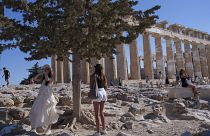 شابة تشرب الماء قرب معبد البارثينون الأثري في يوم حار وعاصف في تلة أكروبوليس، في أثينا 16 تموز/يوليو 2024