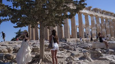 شابة تشرب الماء قرب معبد البارثينون الأثري في يوم حار وعاصف في تلة أكروبوليس، في أثينا 16 تموز/يوليو 2024