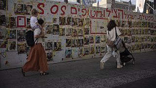 People walk past a wall with photos of hostages held in the Gaza Strip at a plaza known as Hostages Square in Tel Aviv, Israel