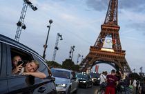 Des passagers à l'arrière d'un taxi se filment alors qu'ils quittent la Tour Eiffel décorée des anneaux olympiques avant les Jeux olympiques d'été de 2024, mercredi 17 juillet 2024.