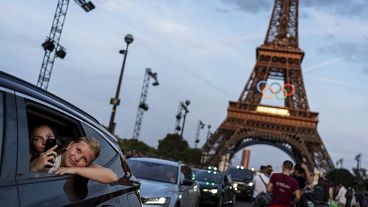 Des passagers à l'arrière d'un taxi se filment alors qu'ils quittent la Tour Eiffel décorée des anneaux olympiques avant les Jeux olympiques d'été de 2024, mercredi 17 juillet 2024.
