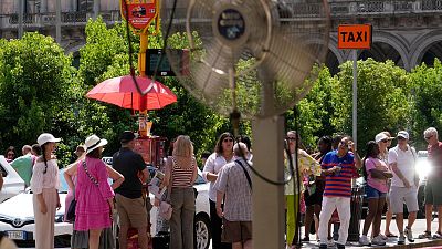 Des touristes attendent un bus sous le soleil à Milan, en Italie, le 16 juillet 2024.