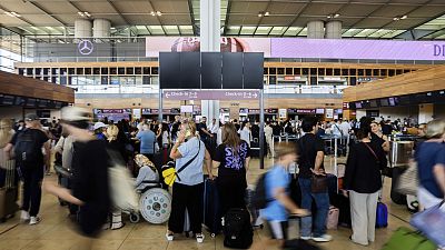 Utasok várakoznak a Berlin-Brandenburg repülőtér üres fekete kijelzőtáblájánál