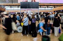 Numerous passengers wait in front of a black display board at the capital's Berlin Brandenburg Airport, in Schönefeld, Germany, Friday July 19, 2024