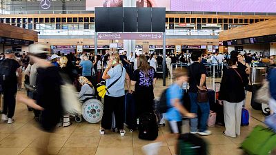 Numerous passengers wait in front of a black display board at the capital's Berlin Brandenburg Airport, in Schönefeld, Germany, Friday July 19, 2024