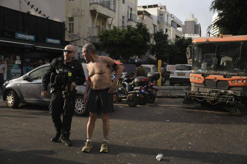 عدّاء يتحدّث مع شرطي إسرائيلي أثناء تحقيقه في مكان انفجار مميت في تل أبيب، إسرائيل (19 يوليو 2024) 