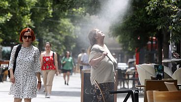 Una mujer intenta refrescarse de una neblina de agua en un día caluroso en Skopje, Macedonia del Norte, el jueves 20 de junio de 2024.
