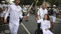 Press agency photographer Christina Assi, right, holds the Olympic torch with. Nicolas Payeur, left, at the 2024 Summer Olympics, Sunday, July 21, 2024,