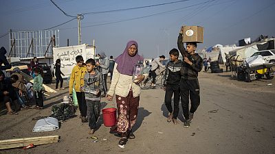 Awatif Abu Jarad, displaced by the Israeli bombardment of the Gaza Strip, carries filled water bottles with her nephews at a makeshift tent camp in Muwasi, 1 January 2024