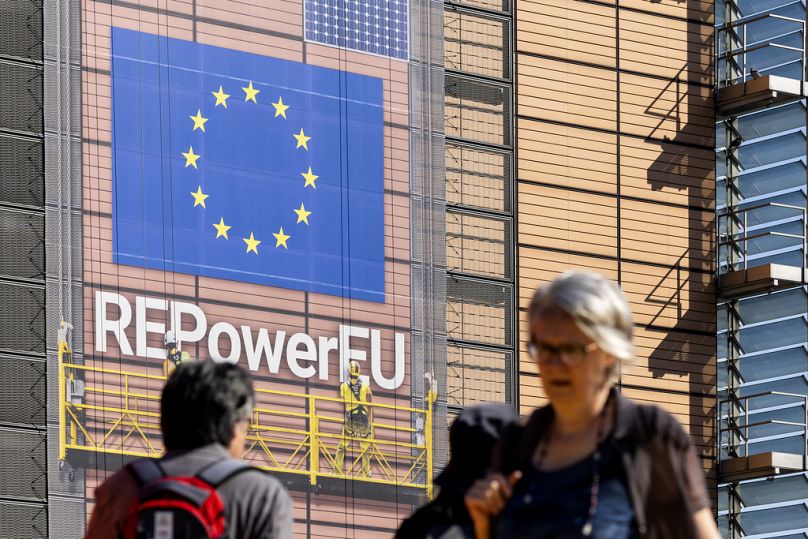  Pedestrians walk in front of a banner outside EU headquarters ahead of an EU summit in Brussels, June 2024