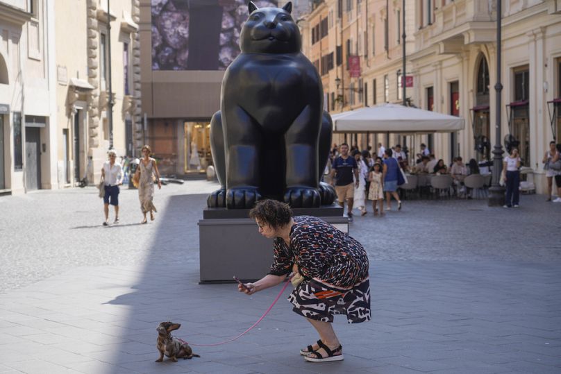 Uma mulher tira uma fotografia ao seu cão diante da escultura “Gato” de Fernando Botero na Piazza San Lorenzo, em Lucina, Roma, no sábado, 20 de julho de 2024.