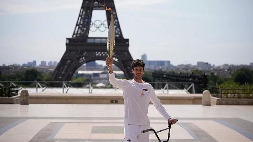 French BMX champion Matthias Dandois holds the Olympic torch in front of the Eiffel Tower