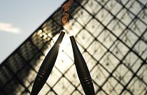 A tocha olímpica é vista durante um revezamento no pátio do Museu do Louvre no domingo, 14 de julho de 2024, em Paris.