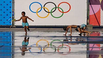 Children play at a splash fountain area near signage for the 2024 Summer Olympics, Tuesday, July 23, 2024, in Nice, France. Nice will host six soccer matches during the summer