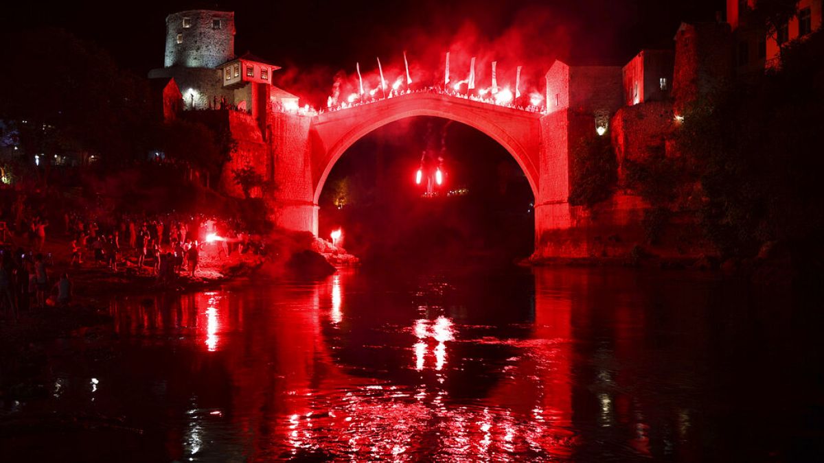 Um mergulhador com tochas salta da Ponte Velha durante um espetáculo noturno em Mostar, na Bósnia, no domingo, 31 de julho de 2024. 