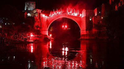 Um mergulhador com tochas salta da Ponte Velha durante um espetáculo noturno em Mostar, na Bósnia, no domingo, 31 de julho de 2024. 