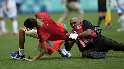 Um comissário de bordo apanha um invasor de campo durante o jogo de futebol masculino entre a Argentina e Marrocos no Estádio Geoffroy-Guichard, nos Jogos Olímpicos de verão de 2024, em Saint-Etienne