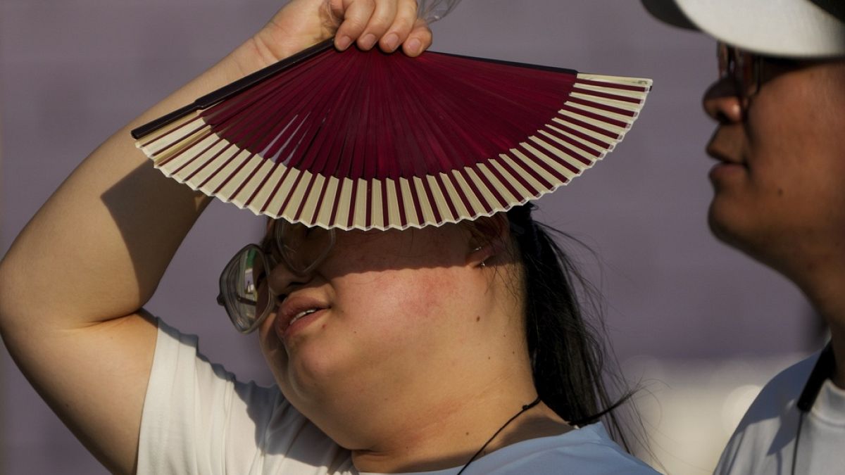 FILE - A woman uses a fan as she walks with her companion on a hot day in Beijing, June 16, 2024