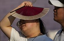 FILE - A woman uses a fan as she walks with her companion on a hot day in Beijing, June 16, 2024