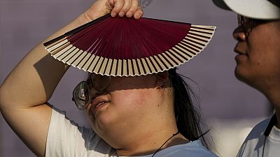 FILE - A woman uses a fan as she walks with her companion on a hot day in Beijing, June 16, 2024