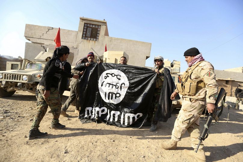 Iraqi Army soldiers celebrate as they hold a flag of the Islamic State group they captured during a military operation to regain control of a village outside Mosul, Iraq.