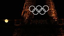 A lua cheia surge por detrás dos anéis olímpicos pendurados na Torre Eiffel