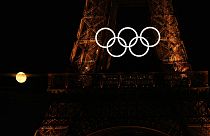 Полная луна поднимается за олимпийскими кольцами, свисающими с Эйфелевой башни в понедельник, 22 июля 2024 года, в Париже, Франция. Церемония открытия Олимпийских игр состоится в пятницу. 