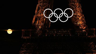 A lua cheia surge por detrás dos anéis olímpicos pendurados na Torre Eiffel