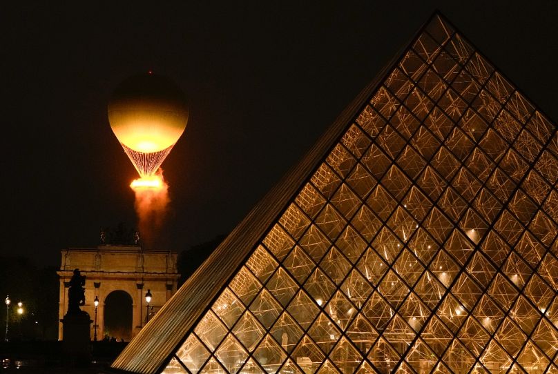 Az olimpiai lángot jelképező hőlégballon a Louvre üvegpiramisa mögött, 2024. július 26-án