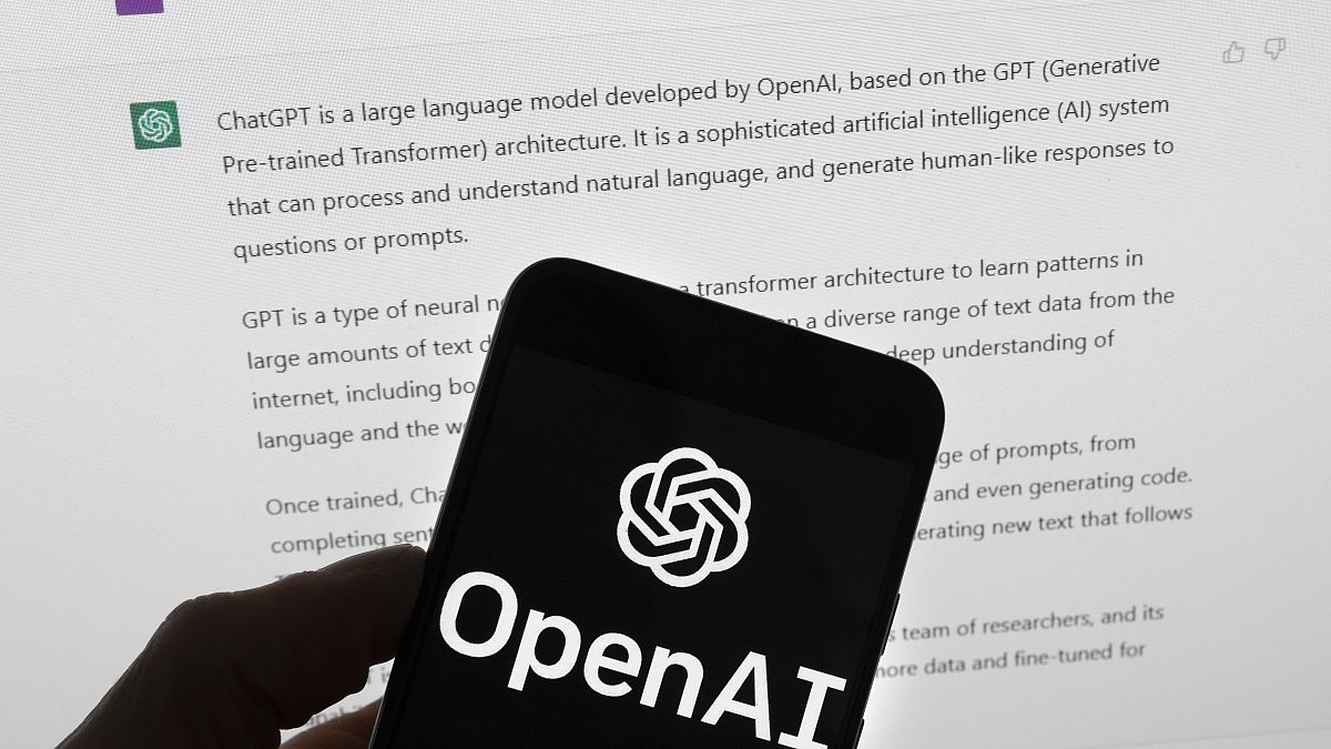 The OpenAI logo is seen on a mobile phone in front of a computer screen which displays output from ChatGPT, Tuesday, March 21, 2023, in Boston. 