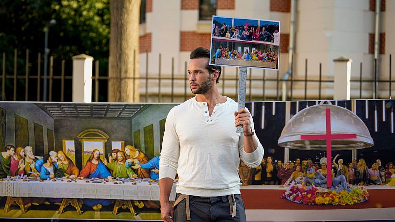 Tristan Tate holds a picture of a scene that took place during the opening ceremony that seemed to evoke Leonardo da Vinci's "The Last Supper" in Bucharest, Romania 