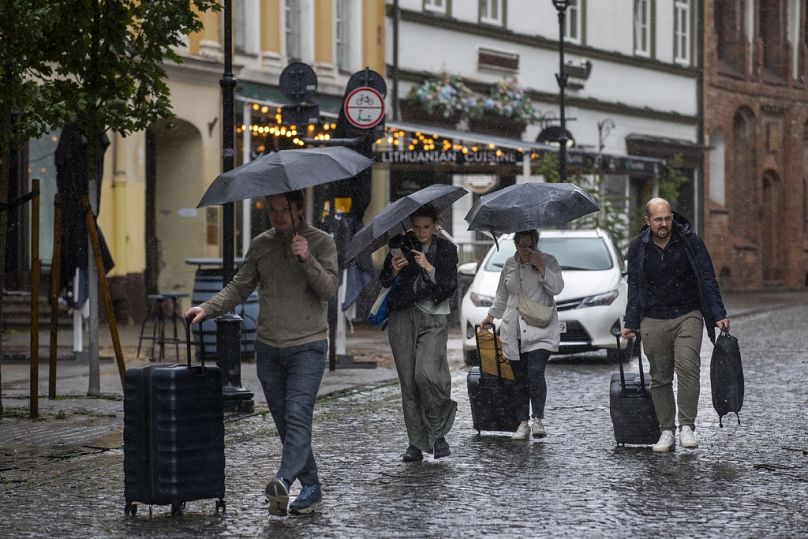 People shelter from the rain under umbrellas on a rainy day, in Vilnius, Lithuania, Monday, July 29, 2024.