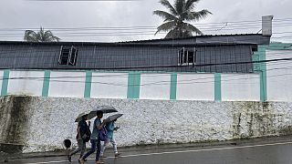 Persone escono al mattino per andare al lavoro tenendo in mano gli ombrelli durante la pioggia a Kochi, nello Stato del Kerala, in India, martedì 30 luglio 2024.