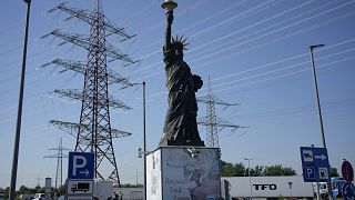 Köln yakınlarında kamyonların park ettiği bir benzin istasyonunda, özgürlük heykelinin bir replikasının arkasında yüksek gerilim direkleri duruyor 