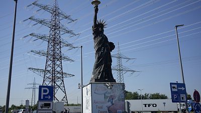 igh voltage pylons stand behind a replica of the statue of liberty, at a petrol station where trucks are parked near Cologne 