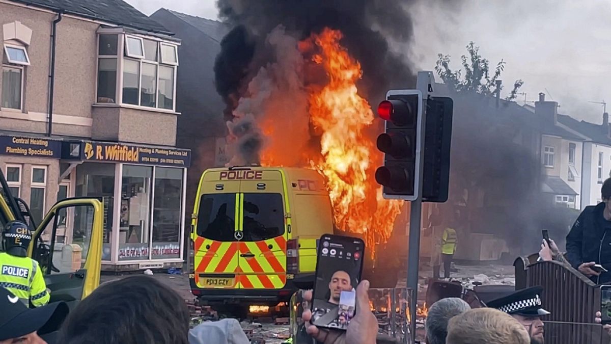 Una furgoneta de la policía bollos como y desordenada multitud se enfrentó con la policía, martes, 30 de julio 2024, en Southport, noroeste de Inglaterra