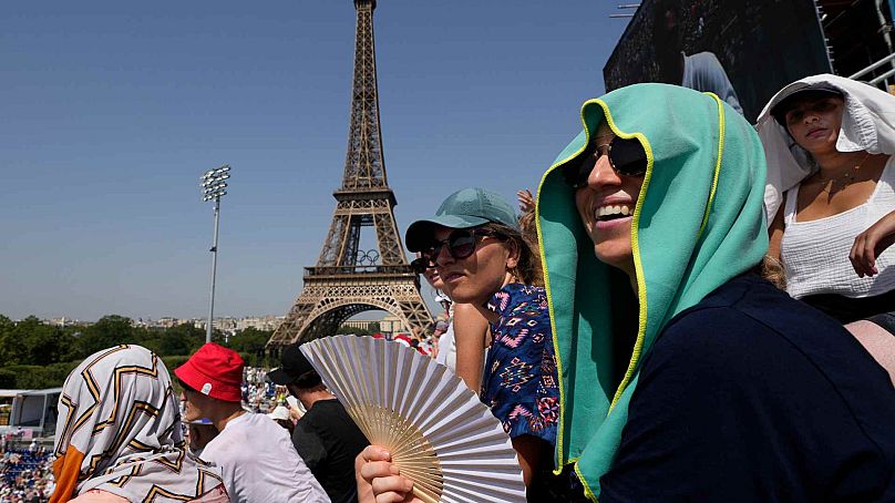 Stephanie Touissaint, foreground, uses a fan to keep cool in the sweltering heat at Eiffel Tower Stadium during a beach volleyball match at the 2024 Summer Olympics