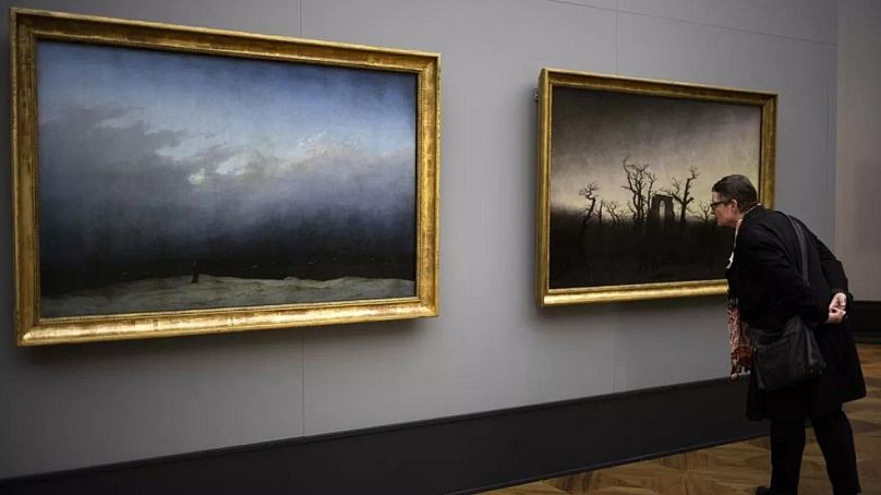 A woman inspects Caspar David Friedrich's painting 'Abby Among The Oaks', displayed next to 'Monk By The Sea' during a press preview.