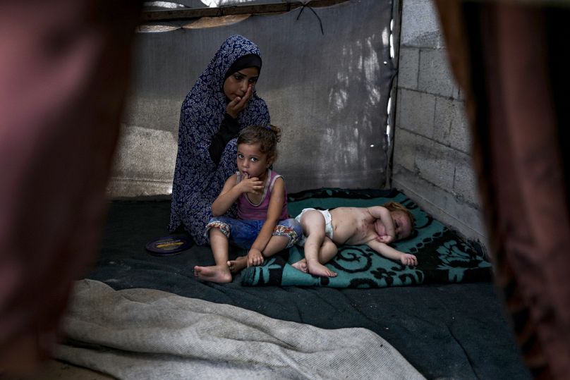 فلسطينية نزحت جرّاء القصف الإسرائيلي، تجلس إلى جانب أطفالها في مخيم مؤقت في دير البلح وسط قطاع غزة (29 يوليو 2024)