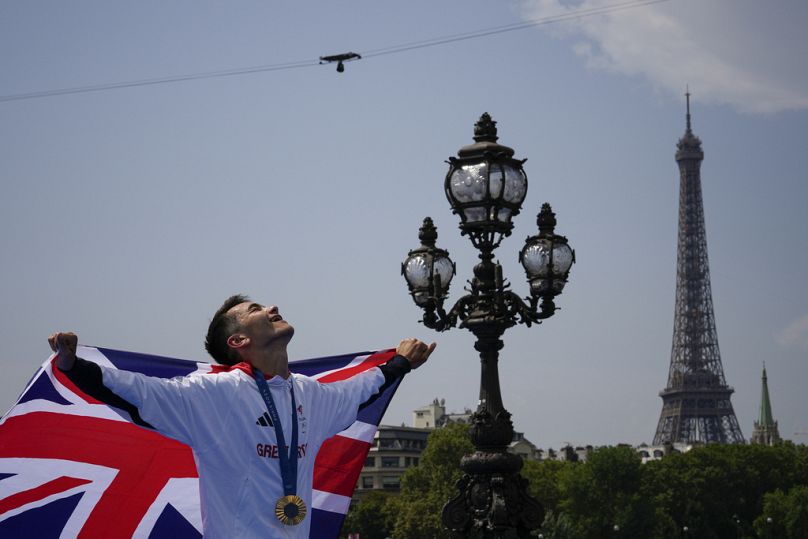 Gold medalist Britain's Alex Yee holds the Union Jack at the end of a medal ceremony for the men's individual triathlon competition at the 2024 Summer Olympics