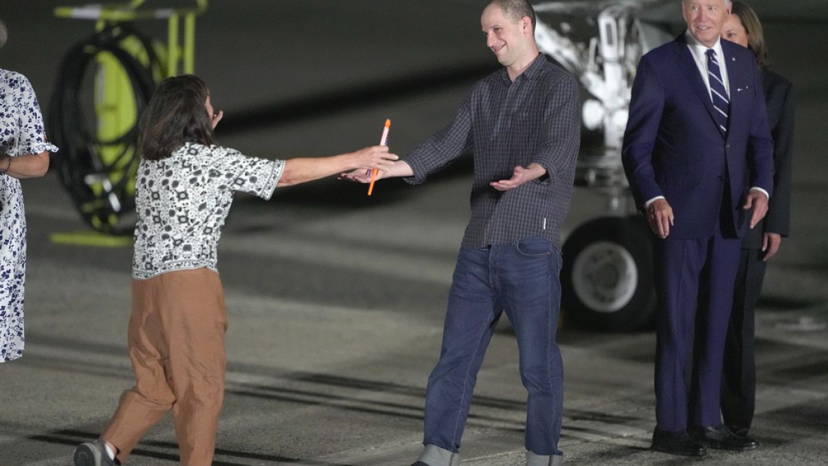 O repórter Evan Gershkovich é recebido na pista pela sua mãe, Ella Milman, enquanto o Presidente Joe Biden e Kamala Harris o observam na Base da Força Aérea de Andrews.